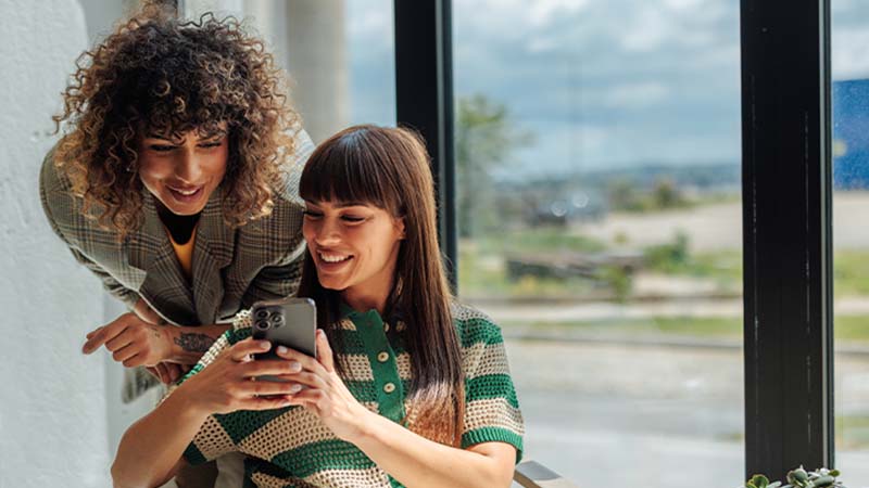 Duas mulheres jovens a consultar redes sociais no telemóvel 